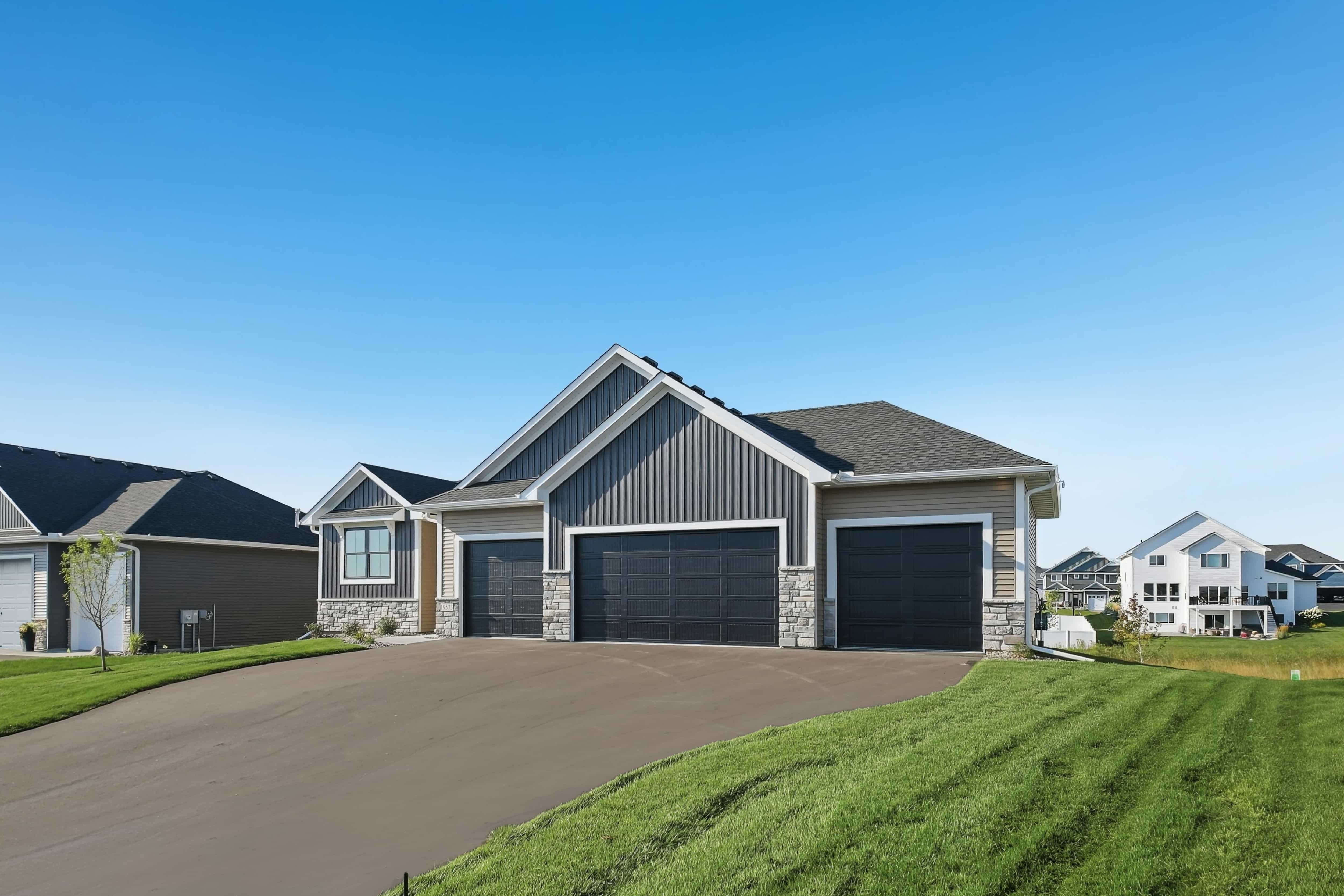 Modern ranch-style home with gray board-and-batten siding, stone accents, and a three-car garage